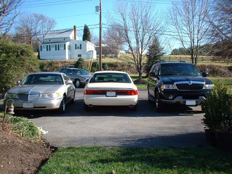 1996 Mercury Grand Marquis - A silver sedan, a cream sedan, and a black SUV are parked in a driveway on a sunny day.