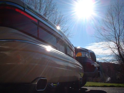1996 Mercury Grand Marquis - Sun glints off the rear of a Mercury Grand Marquis, showing off its exhaust tips and a second vehicle nearby.
