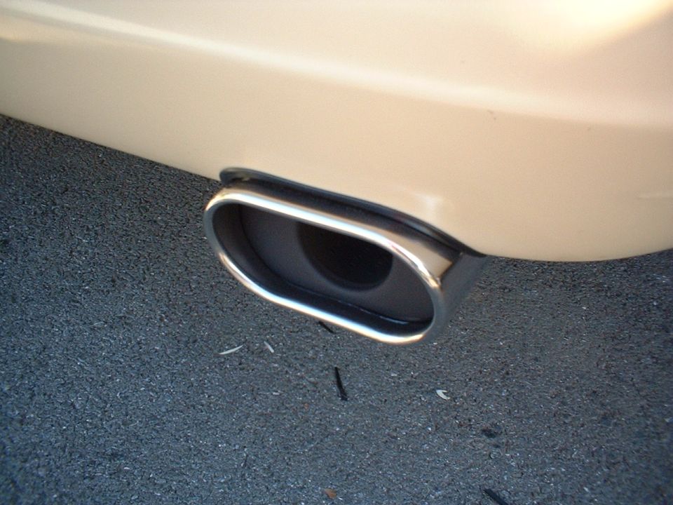 Chrome rectangular exhaust tip on tan bumper over gray pavement