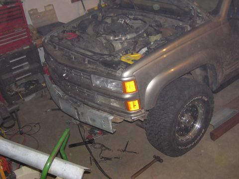 2000 Chevrolet Tahoe - The front bumper of a silver SUV is shown, with the hood open and engine exposed. Tools are scattered around the vehicle.