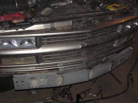 2000 Chevrolet Tahoe - The front of a truck is shown with the hood open, revealing the engine and grille area, with a metal bumper in the foreground.