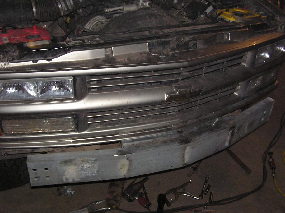 Front end of a truck with grille and headlights visible, and a metal bumper being worked on