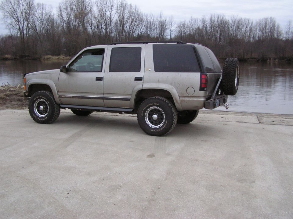 Tan Chevrolet Tahoe SUV with rear tire carrier parked on boat ramp by river