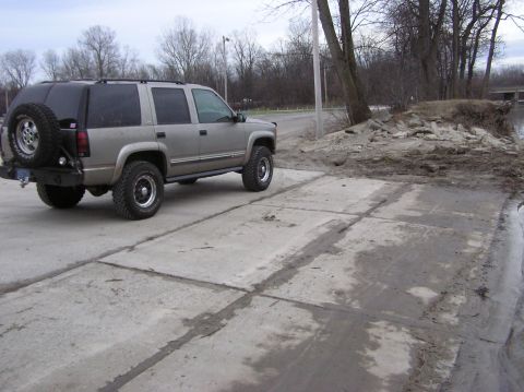 2000 Chevrolet Tahoe - A silver Chevrolet Tahoe with a spare tire mounted on the rear bumper is parked on a concrete surface near a wooded area.