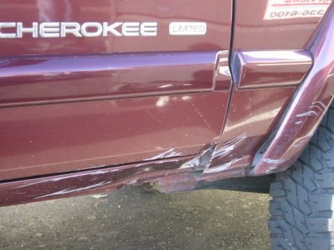 2000 Jeep Cherokee - The side of a Jeep Cherokee Limited shows extensive damage, including dents and scratches along the lower body and rear quarter panel.