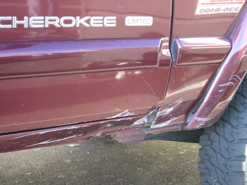 Deep gouges and creased sheet metal on the maroon rocker panel of a Jeep Cherokee Limited