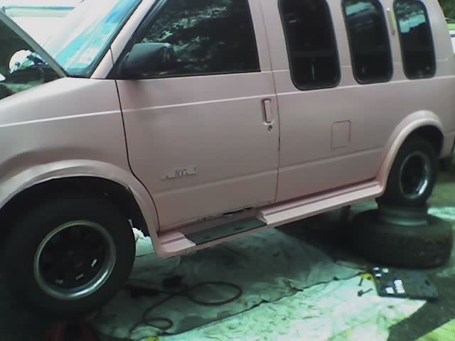 Pink Chevrolet Astro van on jack stands during wheel work