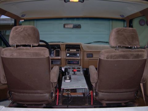 1986 Ford Bronco - The interior of a vehicle shows two brown seats and a custom metal console with various controls.