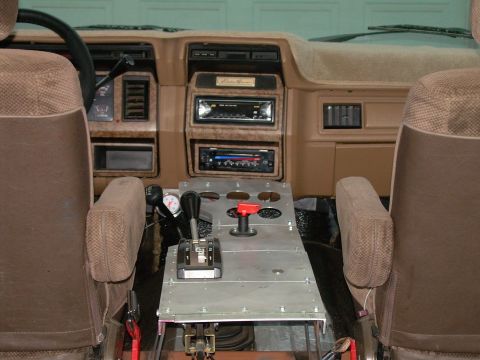 1986 Ford Bronco - The interior of a vehicle shows a custom center console with shifters, gauges, and a red toggle switch.