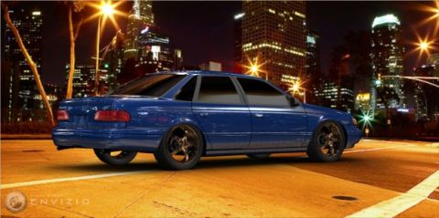 1993 Ford Taurus - A blue 1993 Ford Taurus sedan is captured in a 3/4 rear view at night, with city lights in the background.