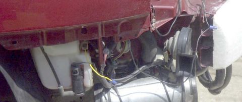1997 Ford Taurus - The front section of a red vehicle reveals its internal wiring, hoses, and a horn assembly.