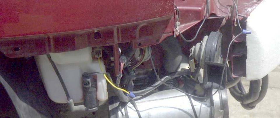 Close-up of wiring, white reservoir and round blower motor under a red vehicle's dash
