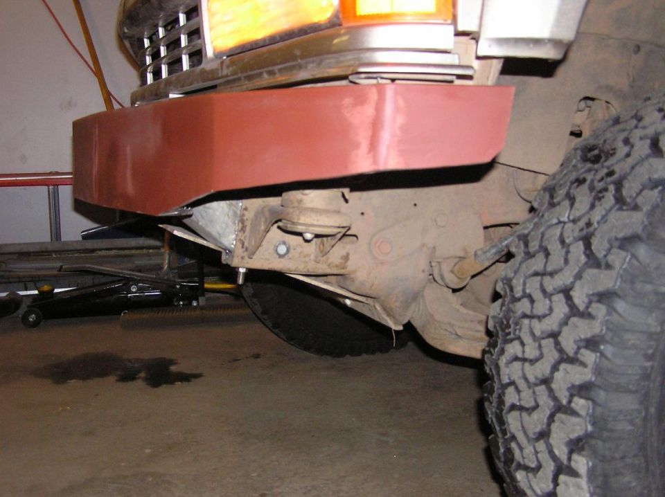 vehicle front end with red primer bumper section, suspension parts, and tire visible