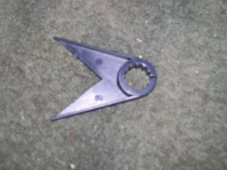 Black V-shaped plastic part with splined collar lying on gray carpet