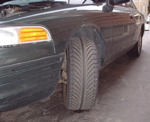 1997 Ford Crown Victoria - The front passenger side of a dark-colored sedan is visible, focusing on the wheel and headlight assembly.