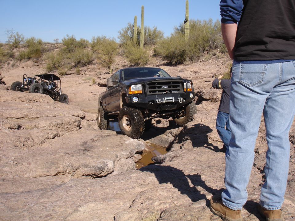 Black Ford truck navigating rocky terrain with a buggy in the background