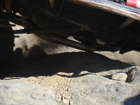 1984 Ford Bronco - The underside of a vehicle is captured in this image, showing its suspension and drivetrain components against a rocky terrain.