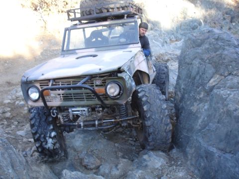 1984 Ford Bronco - Modified SUV with oversized tires navigating a difficult rocky trail.