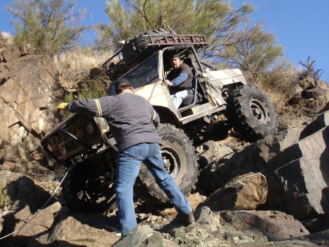 1984 Ford Bronco - A heavily modified off-road vehicle is seen climbing a steep, rocky terrain with assistance from a person on foot.