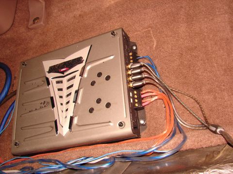 1996 Ford Bronco - A car amplifier with multiple wires connected to its terminals is shown installed on a carpeted surface.