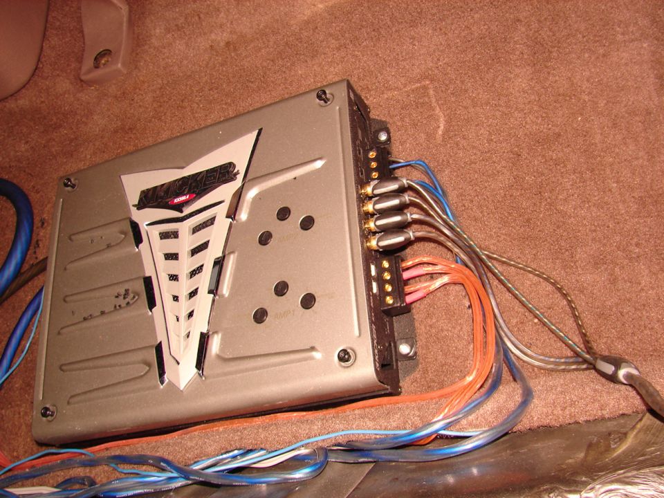 Silver Kicker car amplifier on tan carpet wired with RCA and speaker cables