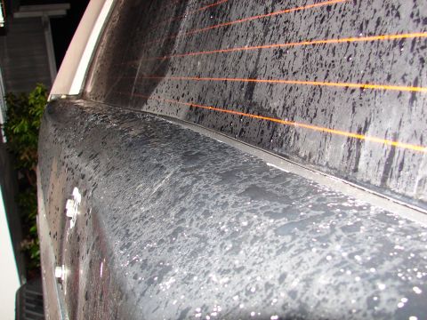 1996 Ford Bronco - Close-up of a vehicle's rear quarter panel and window, covered in water droplets.