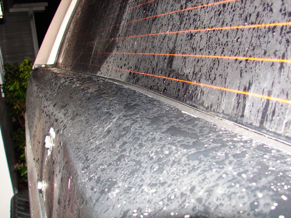 Black vehicle rear quarter panel with water droplets and orange defroster lines on the window