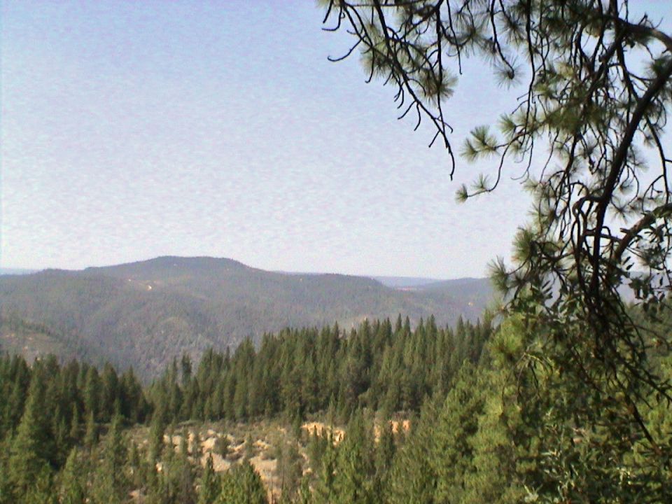 Mountain landscape with pine trees and a clear sky, Supermotors logo in corner