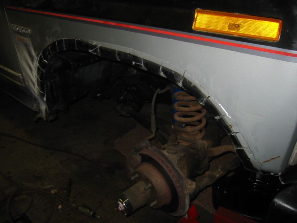 Vehicle's front wheel well with cut fenders and exposed suspension. Gray body with red stripe
