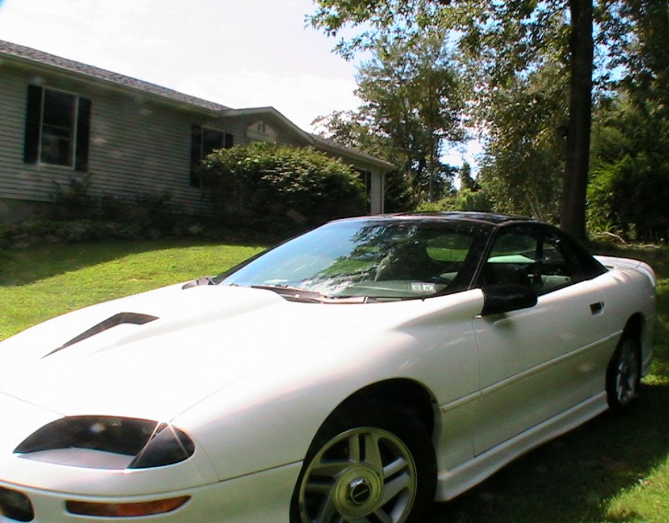 White 1996 Chevrolet Camaro convertible with a black top parked on a grassy lawn in front of a house