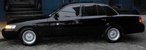 1999 Mercury Grand Marquis - Side view of a black sedan with distinctive aftermarket wheels.