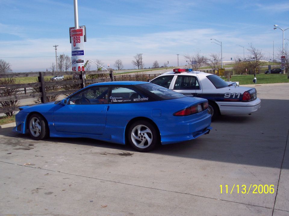 Blue coupe with aftermarket body kit parked next to a police car