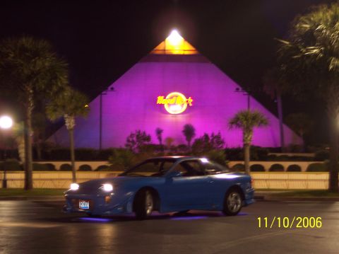 1995 Ford Probe - A blue sports coupe is parked at night in front of a brightly lit Hard Rock Cafe.