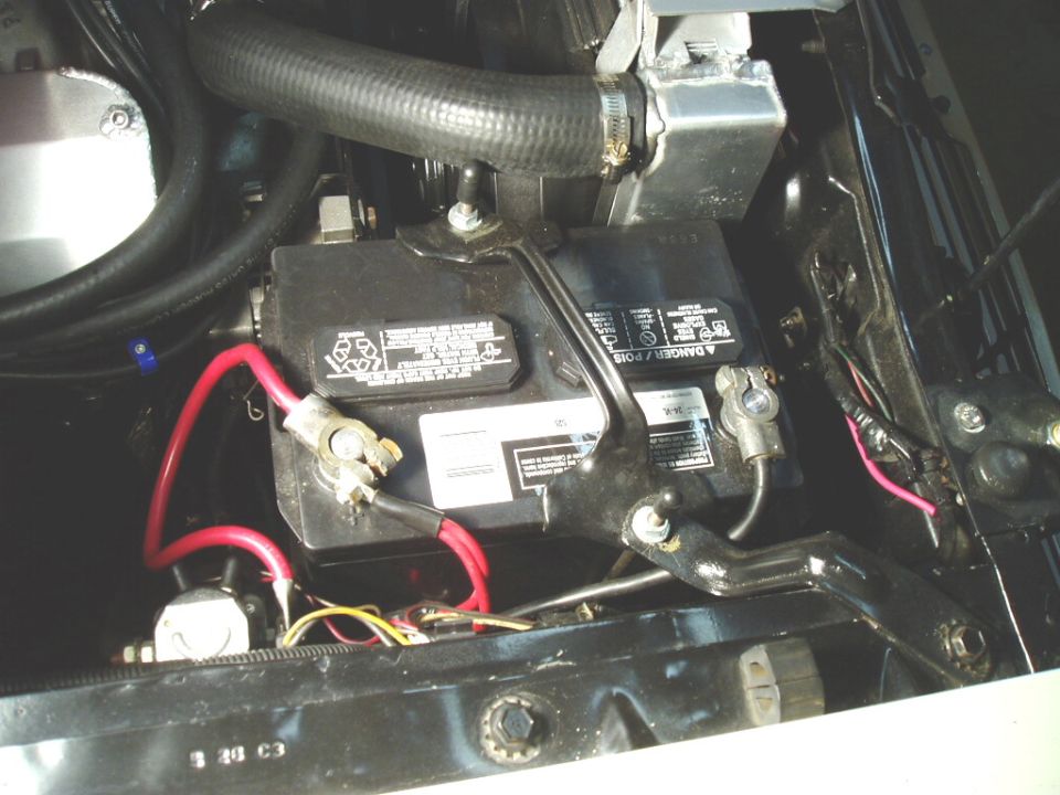 Engine-bay close-up of a black battery in its tray with red and black cable terminals