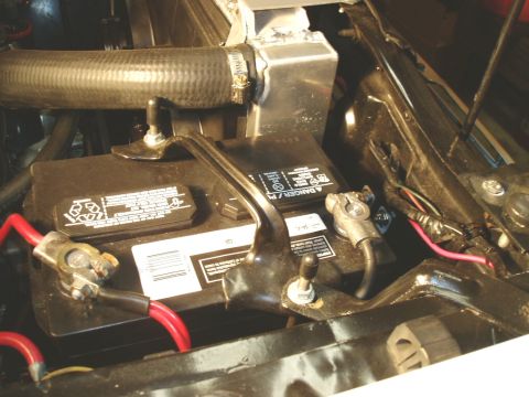 1966 Ford Fairlane - Close-up view of a car battery and radiator hose under the hood of a vehicle.