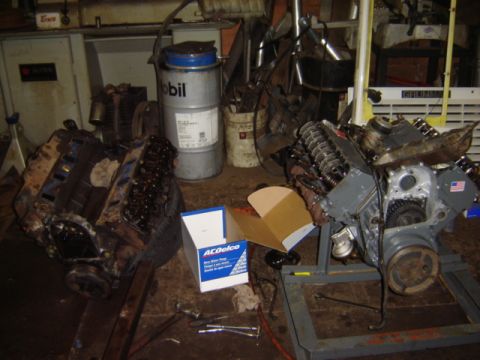 1992 Ford Bronco - Two V8 engines are shown in a workshop setting, with one on a stand and the other on the floor next to a large Mobil oil drum.
