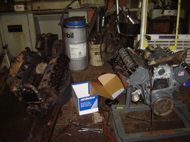 Two V8 engines are in a garage, one on the floor and one on a stand. A box of ACDelco parts is nearby