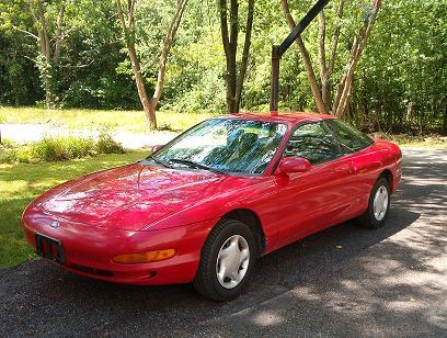 1995 Ford Probe - A red 1995 Ford Probe is parked outdoors on a paved surface with trees in the background.
