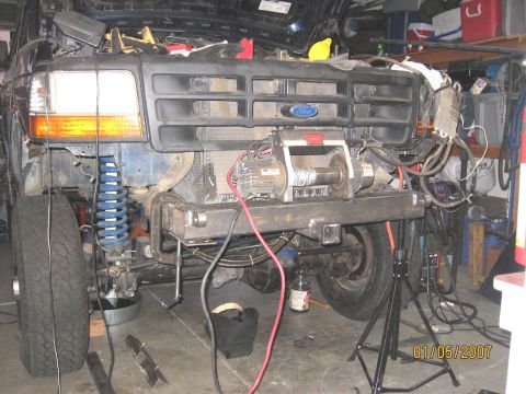 1994 Ford Bronco - The front of a blue 1992 Ford Bronco is disassembled, revealing its engine and suspension components, with a winch attached to the bumper.