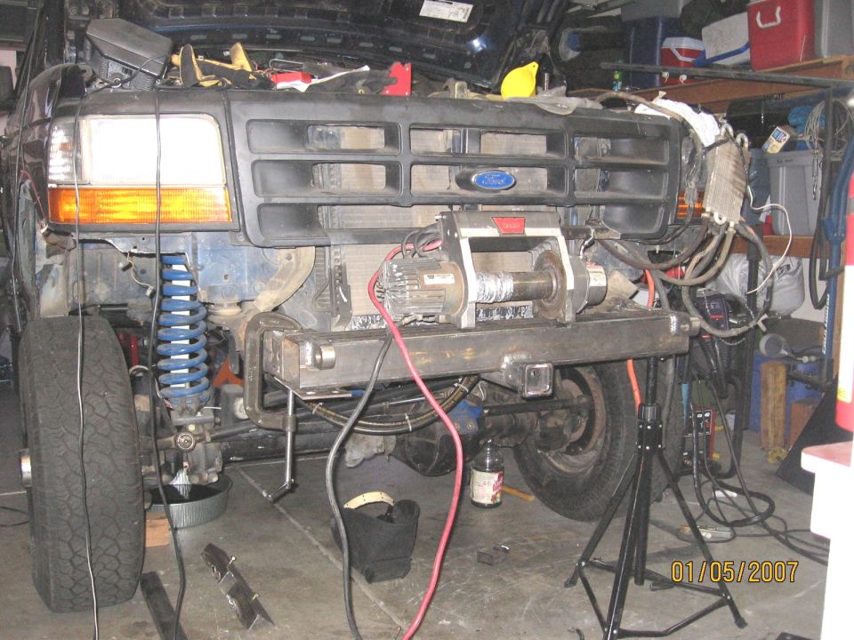 Blue Ford truck front end stripped in garage with winch on bare steel bumper