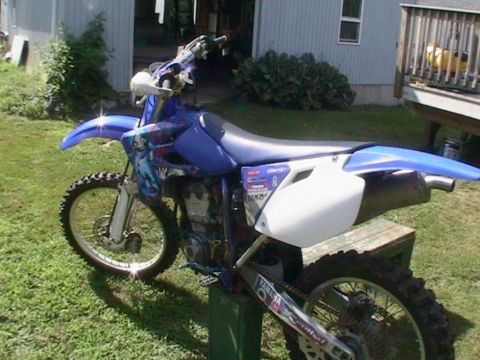 1977 Ford F-250 - A blue dirt bike is parked on grass in front of a house and deck.