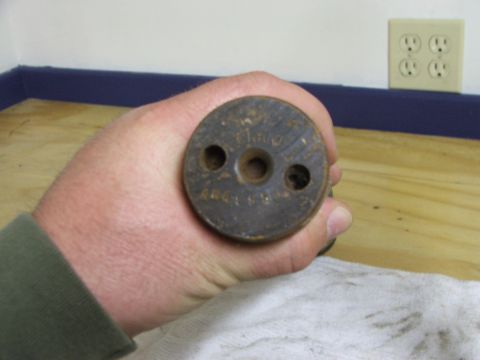 1965 Ford Mustang - A hand holds a round metal part with three holes, possibly a component from a vehicle.
