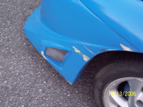 1995 Ford Probe - Close-up of a blue car's front fender with a mesh vent and visible paint chips.