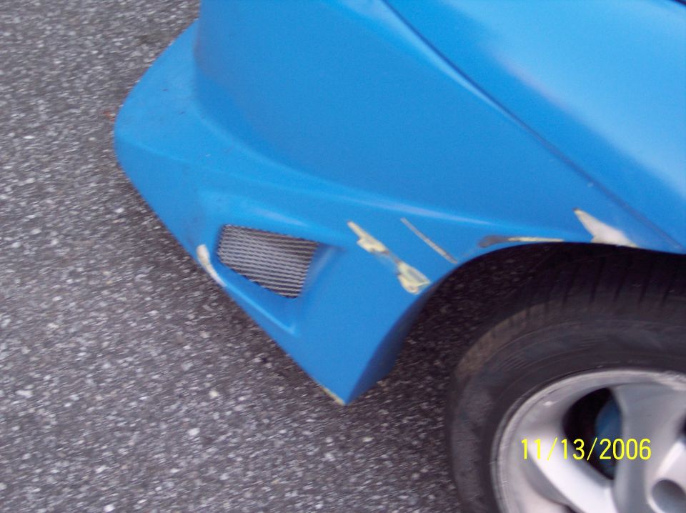 Close-up of a blue car's front fender showing a mesh vent and some paint damage