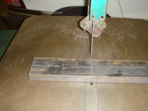 1996 Ford Bronco - A white SUV is partially visible in the background, with its taillight showing, as a metal bar is cut on a band saw.