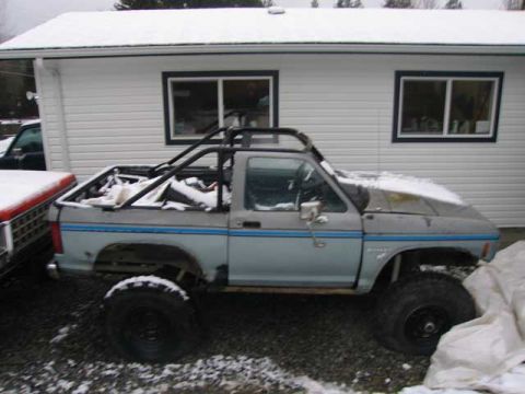 1984 Ford Bronco II - A light blue pickup truck with a roll cage in the bed sits outside a house in the snow.