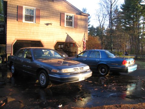 1991 Ford LTD Crown Victoria - Two Ford Crown Victorias are parked in a driveway in front of a house.