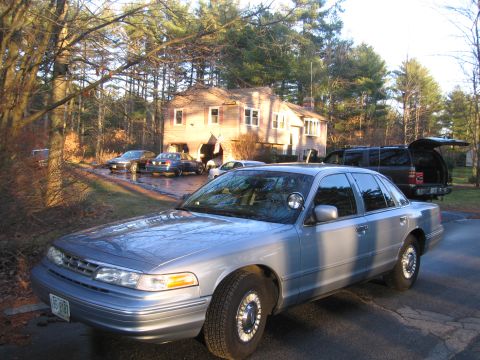 1991 Ford LTD Crown Victoria - A silver sedan, possibly a police vehicle, is parked in a driveway with a house and trees in the background.