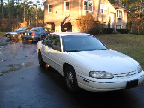 1991 Ford LTD Crown Victoria - Three sedans are parked in a driveway in front of a house on a sunny day.