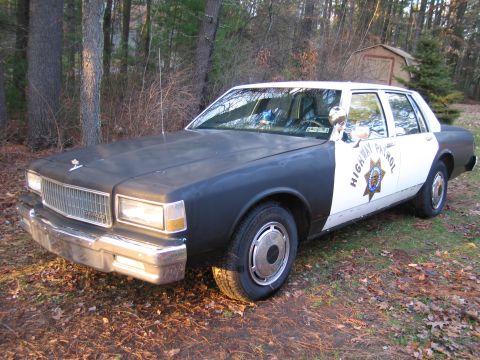 1991 Ford LTD Crown Victoria - This police car, likely from the 1980s, is parked outdoors with a shed in the background.
